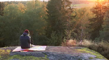 Kvinna tittar i mobilen på bergknalle framför en skog