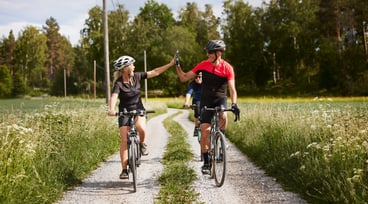 En kvinna och en man cyklar bredvid varandra och gör en high five.