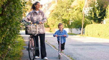 Kvinna leder sin cykel bredvid en pojke på sparkcykel.