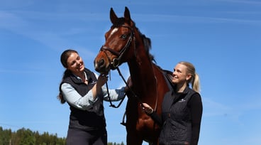 Mathilda och Frida står på varsin sida om en häst med blå himmel i bakgrunden