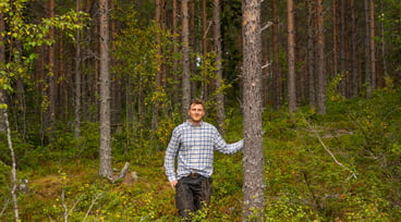 Man står i skogen med ena handen på en trädstam