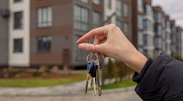 En hand håller upp nycklar framför ett hus