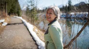 Kvinna med grått hår promenerar på en stig bredvid en sjö