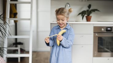 En flicka skalar en banan i köket.