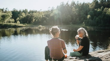 Två äldre kvinnor sitter på en klippa vid vattnet och fikar.
