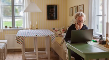 Kvinna sitter vid dator och håller en telefon i handen