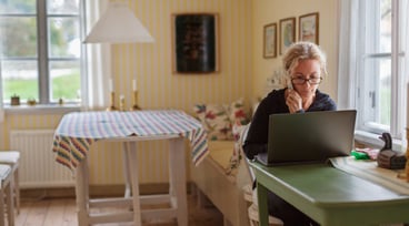 Kvinna sitter vid en dator och jobbar i sitt kök