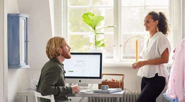 Man sitter framför datorn. Kvinna står bredvid.