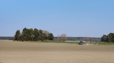 Vy över åker och blå himmel, traktor och såmaskin på avstånd
