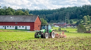 En grön traktor som plöjer en åker