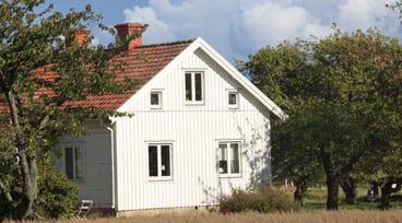 Vitt hus på landsbygden omringat av sädesfält och fruktträd.