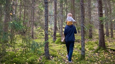 Man promenerar i skogen med barn på axlarna