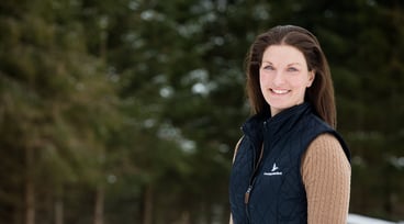 En leende kvinna framför en granskog