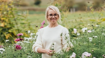 Anna Dymling står i en grönskande trädgård