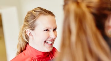 Leende kvinna med röd blus och uppsatt blont hår tittar ut ur bild