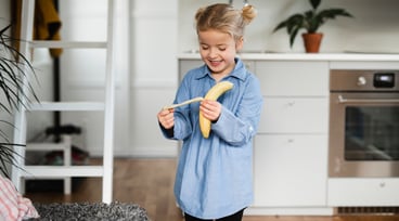 Flicka står i ett kök och äter en banan