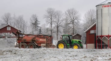 En snöklädd bondgård med en traktor som drar ett släp