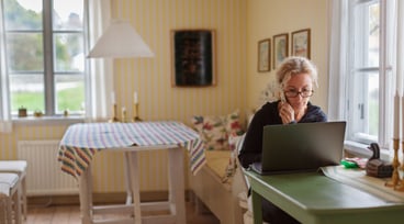 Kvinna sitter vid dator och håller en telefon i handen