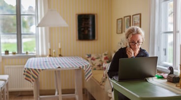 Kvinna sitter vid en dator och jobbar i sitt kök