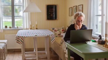 Kvinna sitter vid dator och håller en telefon i handen