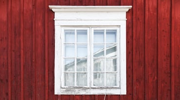 Närbild på röd husvägg och ett vitmålat spröjsat fönster.