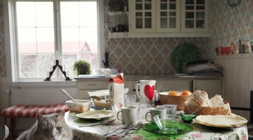 Kök med uppdukad frukost på ett bord och katt som sitter på en stol vid bordet