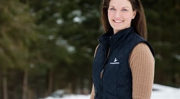 En kvinna står i snön framför en skog. Hon har på sig en väst med Landshypoteks logga.