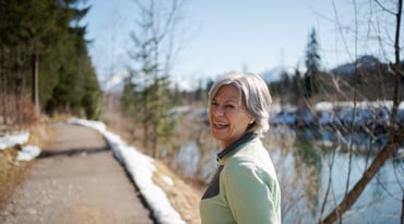 Kvinna med grått hår promenerar på en stig bredvid en sjö