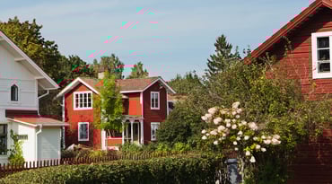 Villakvarter med vita och röda hus. Grönskande trädgård i förgrunden.