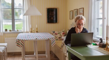 Kvinna sitter vid dator och håller en telefon i handen