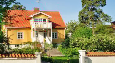 Gult hus med vit veranda och grönskande trädgård utanför Stockholm