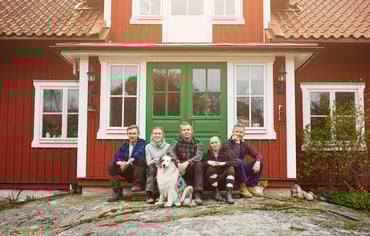 En familj sitter tillsammans framför ett rött hus med grön dörr