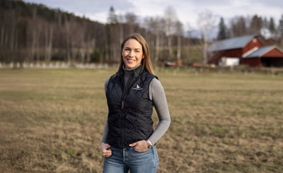 Anna Östlund står på ett fält med ladugårdsbyggnad i bakgrunden