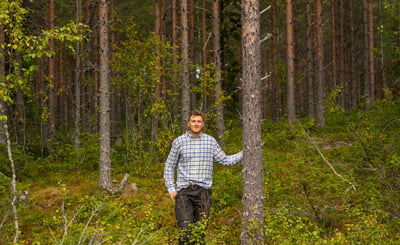 Man står i skogen med ena handen på en trädstam
