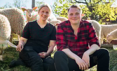 Carl-Johan och Sara sitter framför en grupp får.