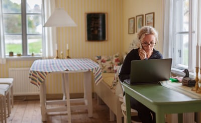 Kvinna sitter vid dator och håller en telefon i handen