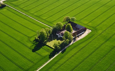 Flygfoto över gård omgiven av klargröna åkrar