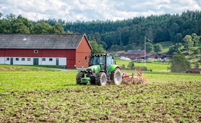 En grön traktor som plöjer en åker