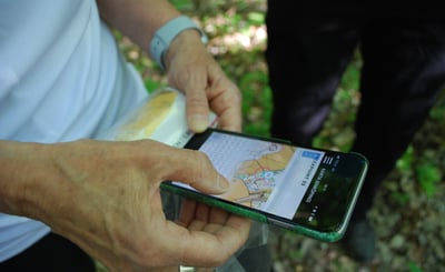 Närbild på händer som håller i mobil, orienteringskarta syns på skärmen