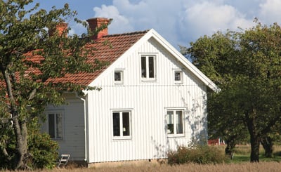 Vitt hus på landsbygden omringat av sädesfält och fruktträd.
