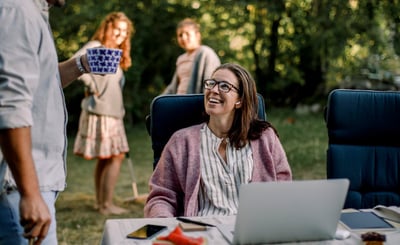 Leende kvinna sitter vid dator och tittar upp mot en man.
