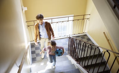 En man och en liten flicka går uppför en trappa i ett lägenhetshus