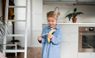 Flicka står i ett kök och äter en banan