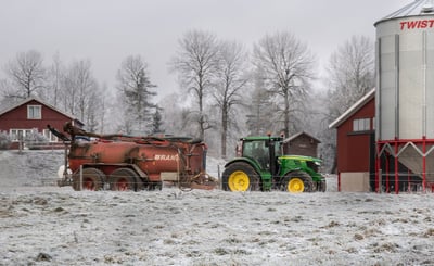 En snöklädd bondgård med en traktor som drar ett släp