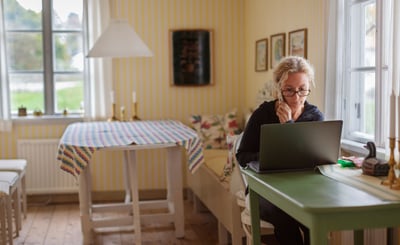 Kvinna sitter vid dator och håller en telefon i handen