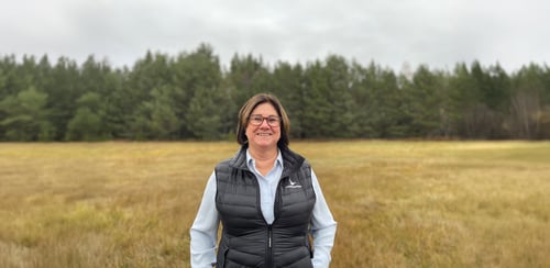 Katarina står framför ett stort fält med skog i bakgrunden