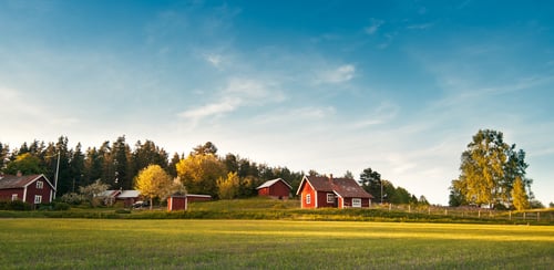 Grön äng framför röda hus med vita knutar. Blå himmel med lätta moln ovanför