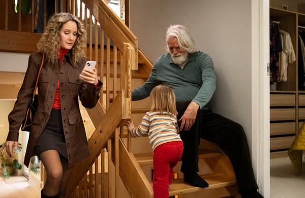 Kvinna går upp i en trappa, bredvid sitter ett barn och en äldre man på ett trappsteg.