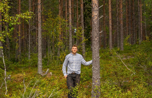Man står i skogen med ena handen på en trädstam