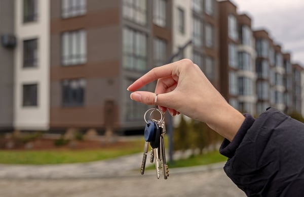 En hand håller upp nycklar framför ett hus